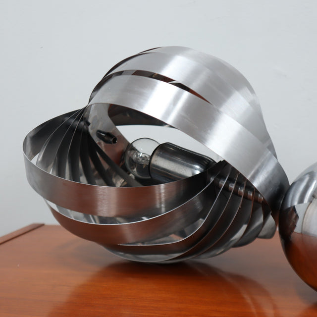 Pair of 1970s Henri Mathieu French kinetic spiral table lamps in brushed steel and chrome illuminated on a wooden sideboard.