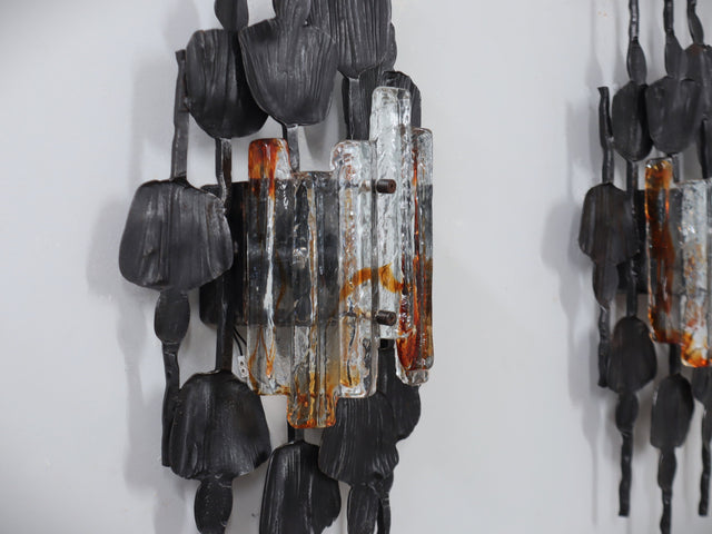 1970s Italian Brutalist lighting, this set of three wall lamps combines sculptural rigor with the refined elegance of Venetian glassmaking. Each piece features a solid, hand-crafted metal structure with bold geometric contours and a raw, expressive surface texture