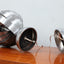 Pair of 1970s Henri Mathieu French kinetic spiral table lamps in brushed steel and chrome illuminated on a wooden sideboard.